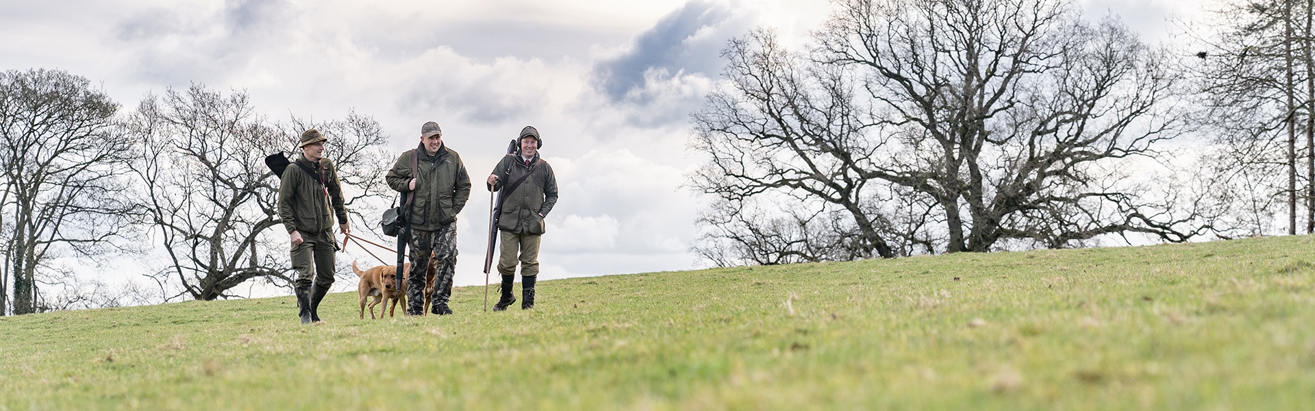 Three game shooters walking across a field with their gundog