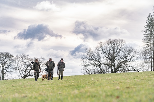 Three game shooters walking across a field with their gundog