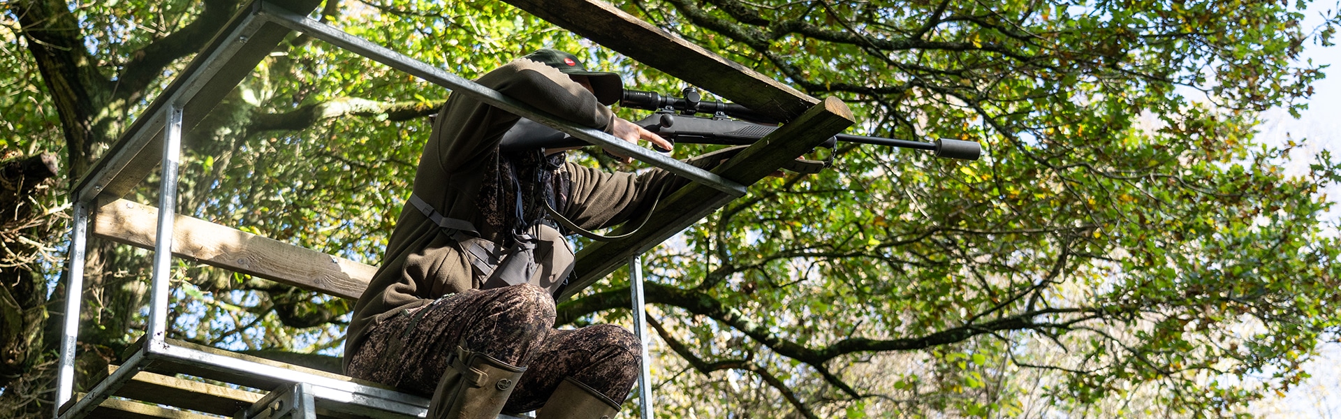 A deer stalking aiming their rifle whilst sitting in a high seat