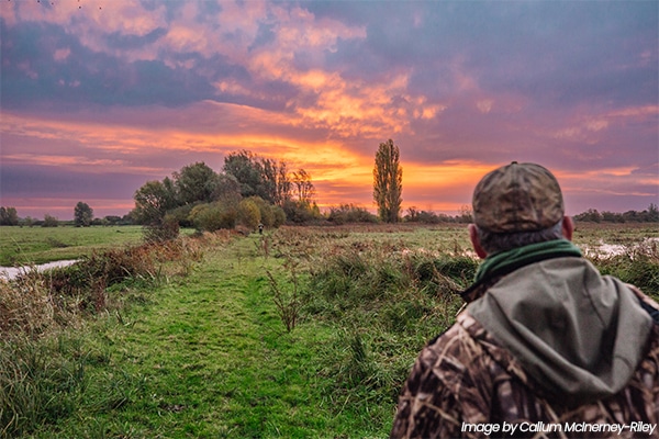 A wildfowler looking across a field at dawn