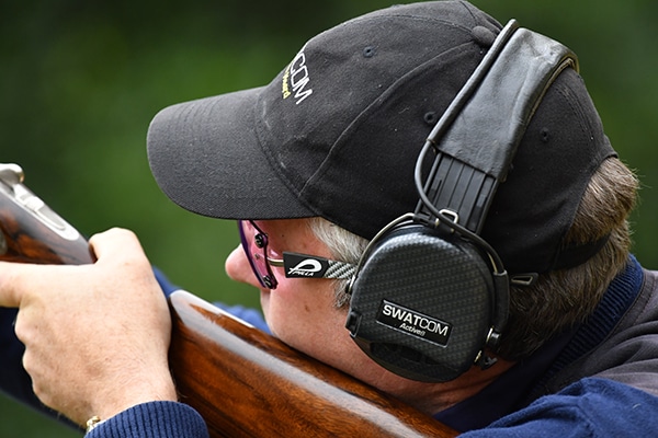 A shooter aiming a shotgun wearing hearing protection